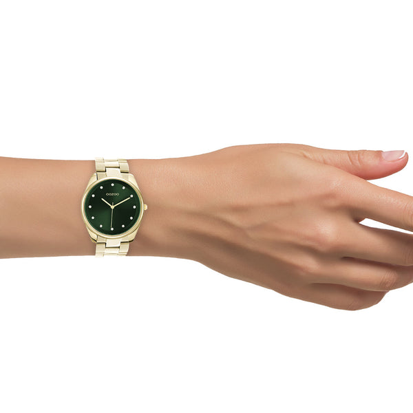 goudkleurige ronde oozoo met steentjes op groene wijzerplaat | stainless steel